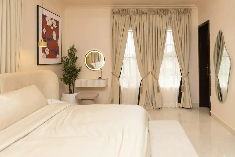 Beige pleated curtains framing tall windows in a bright bedroom