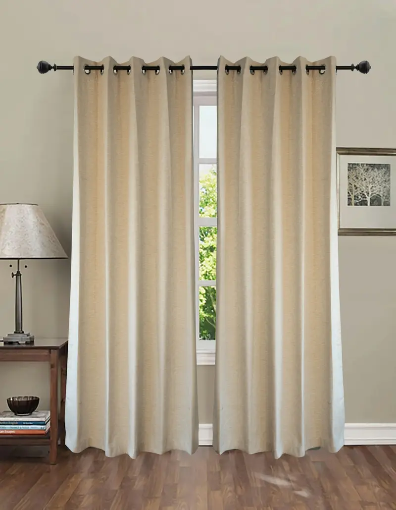 Beige eyelet curtains hanging from a black rod beside a window and table lamp
